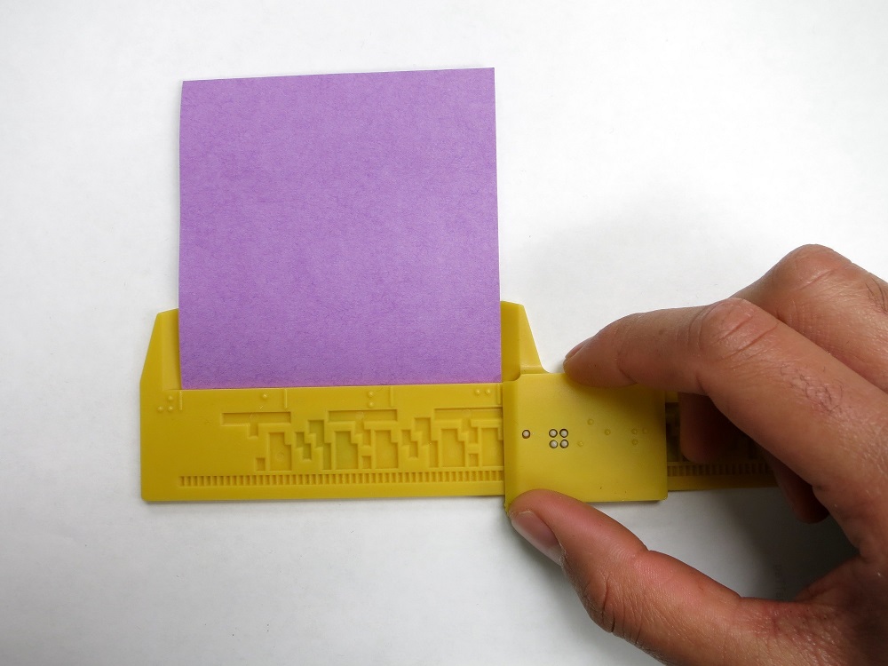 shows the 12-inch Braille Caliper being used to measure a piece of paper